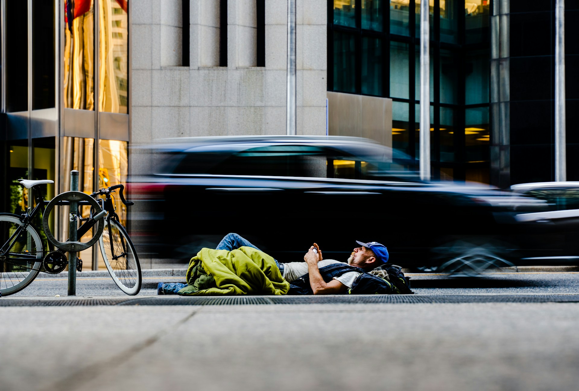 Man laying down on the street near a black car